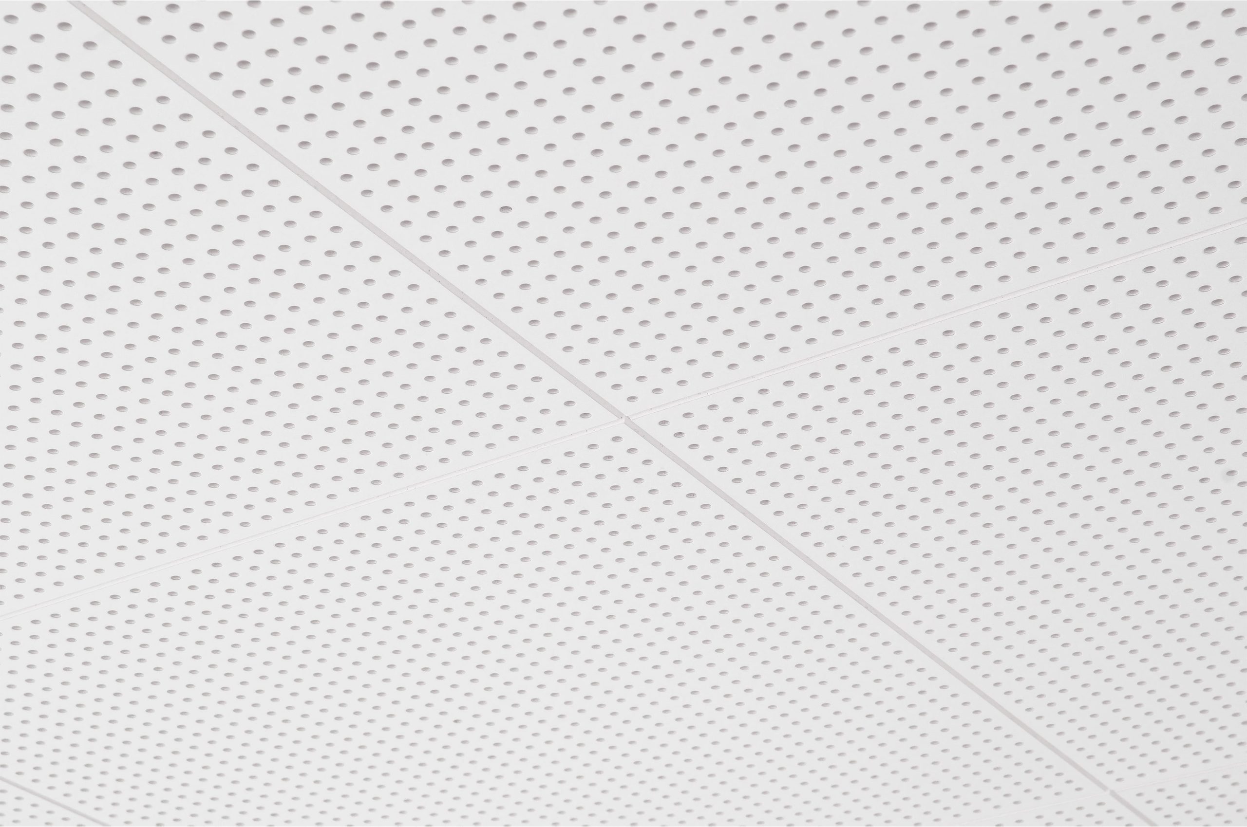 Close-up view of a white perforated ceiling with a grid pattern, showing intersecting lines and evenly spaced small round holes on each ceiling panel.