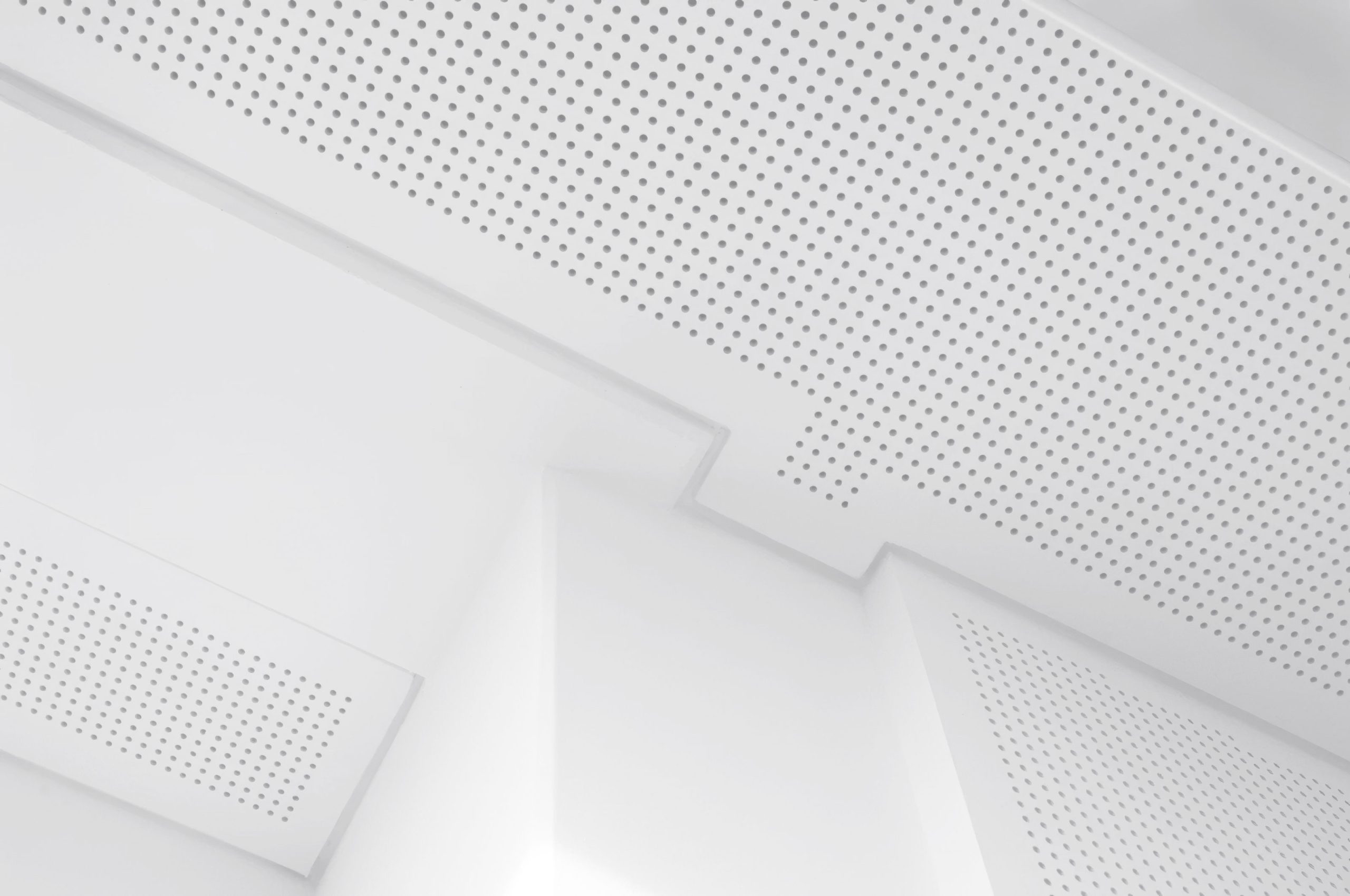 White perforated ceiling panels arranged geometrically, creating a modern, minimalist architectural look with clean lines and soft lighting.