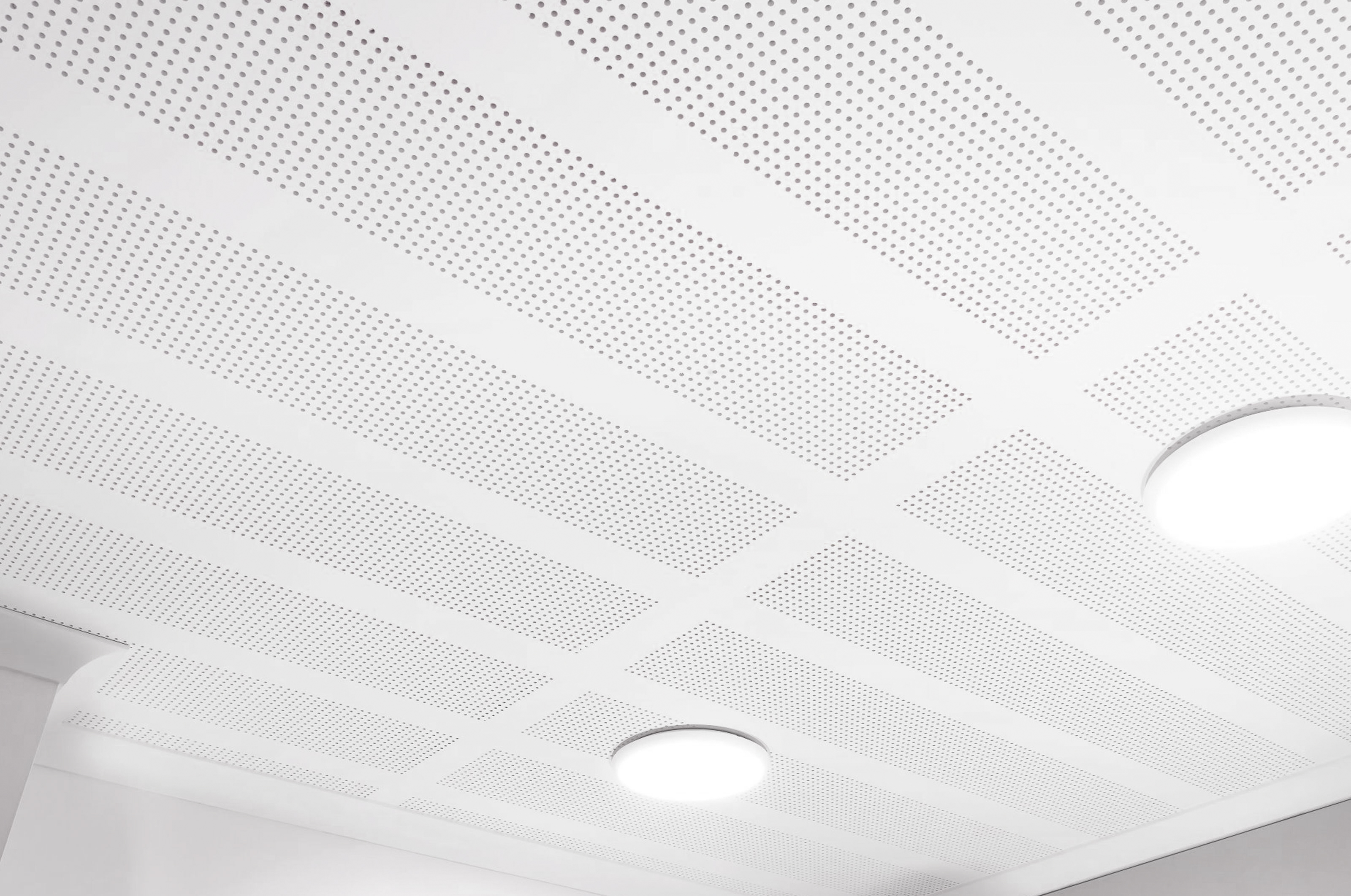 A white, perforated ceiling with a grid pattern and two round, recessed light fixtures glowing softly. The image is bright and minimalistic.