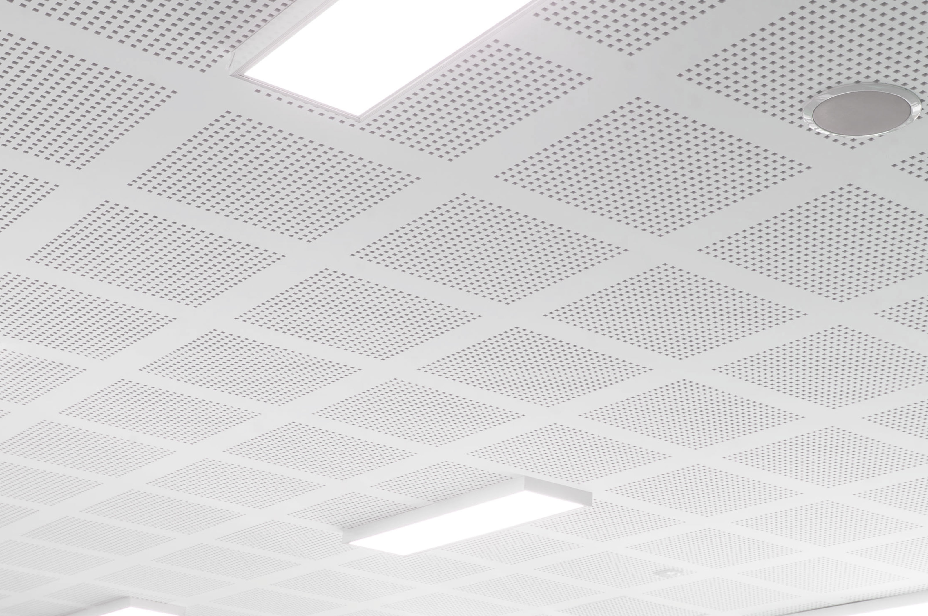 A white ceiling with a grid of perforated square panels, circular speaker, and rectangular fluorescent lights embedded in the surface. The overall appearance is clean and modern.