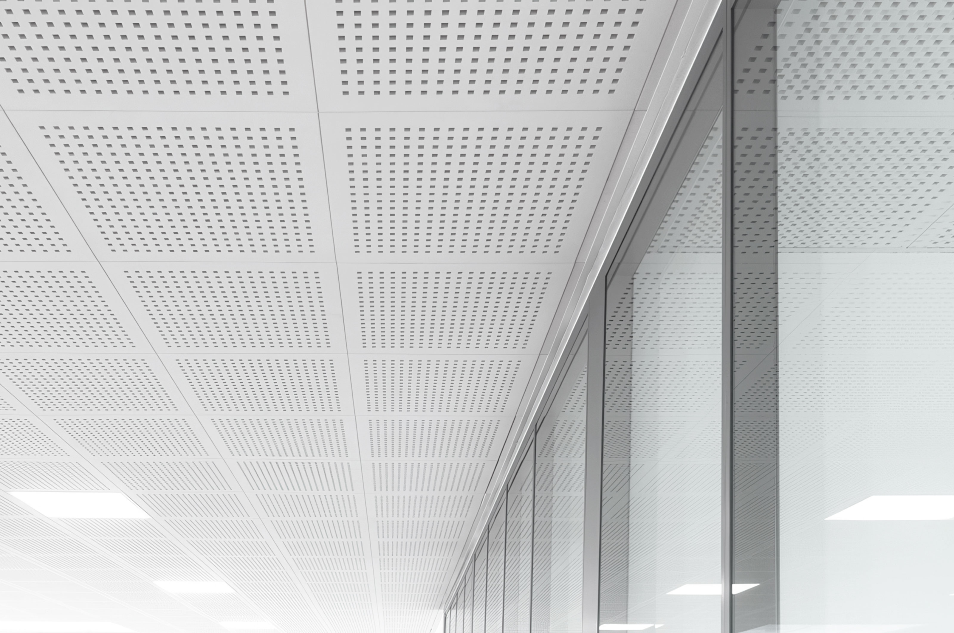 A modern, minimalist ceiling with square perforated panels and bright lighting, reflected in a large glass wall on the right side of the image. The scene is clean, sleek, and mostly white.