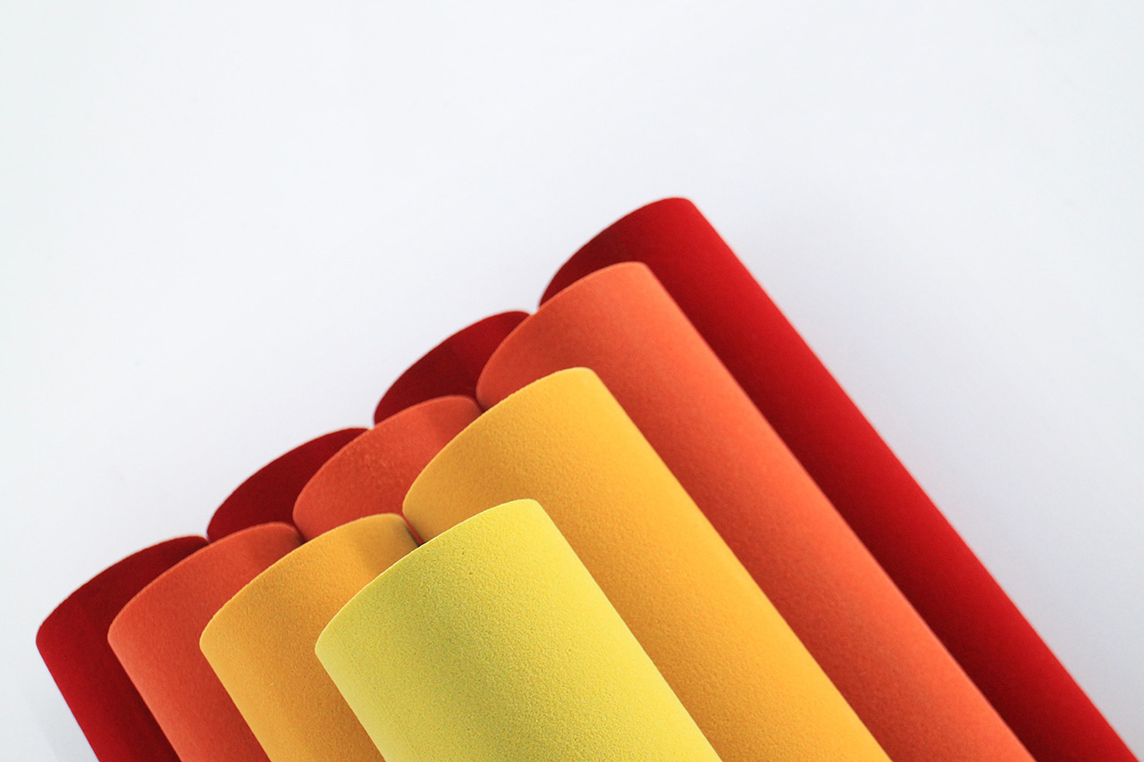 Several sheets of textured paper or material in shades of yellow, orange, and red are rolled up and arranged diagonally against a plain white background.