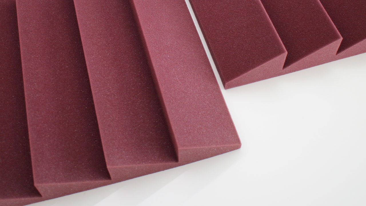 Close-up view of maroon-colored acoustic foam panels with ridged, triangular patterns arranged on a white surface.