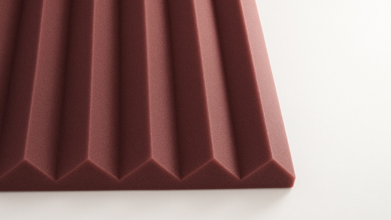 Close-up view of a maroon acoustic foam panel with a series of evenly spaced, triangular ridges, placed on a white surface.