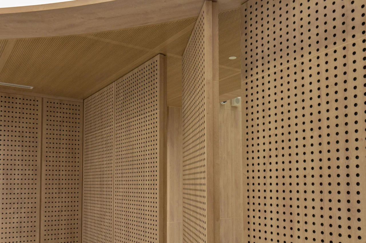 Interior walls and ceiling covered with light wood panels featuring a grid of round perforations, creating a modern and textured architectural design.