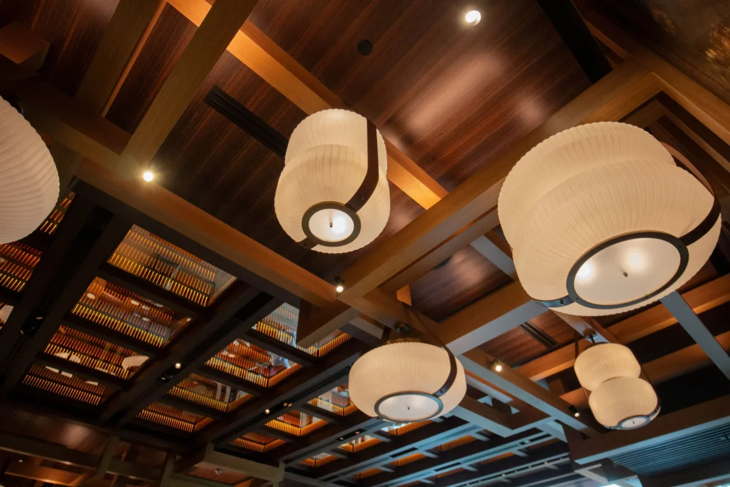 Large, round, white pendant lights hang from a wooden ceiling with geometric beams and recessed lighting, creating a warm and inviting atmosphere.
