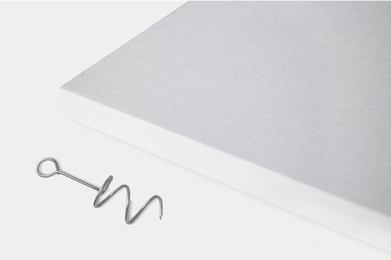 A metal corkscrew lies next to the corner of a thick white rectangular board on a plain white background.