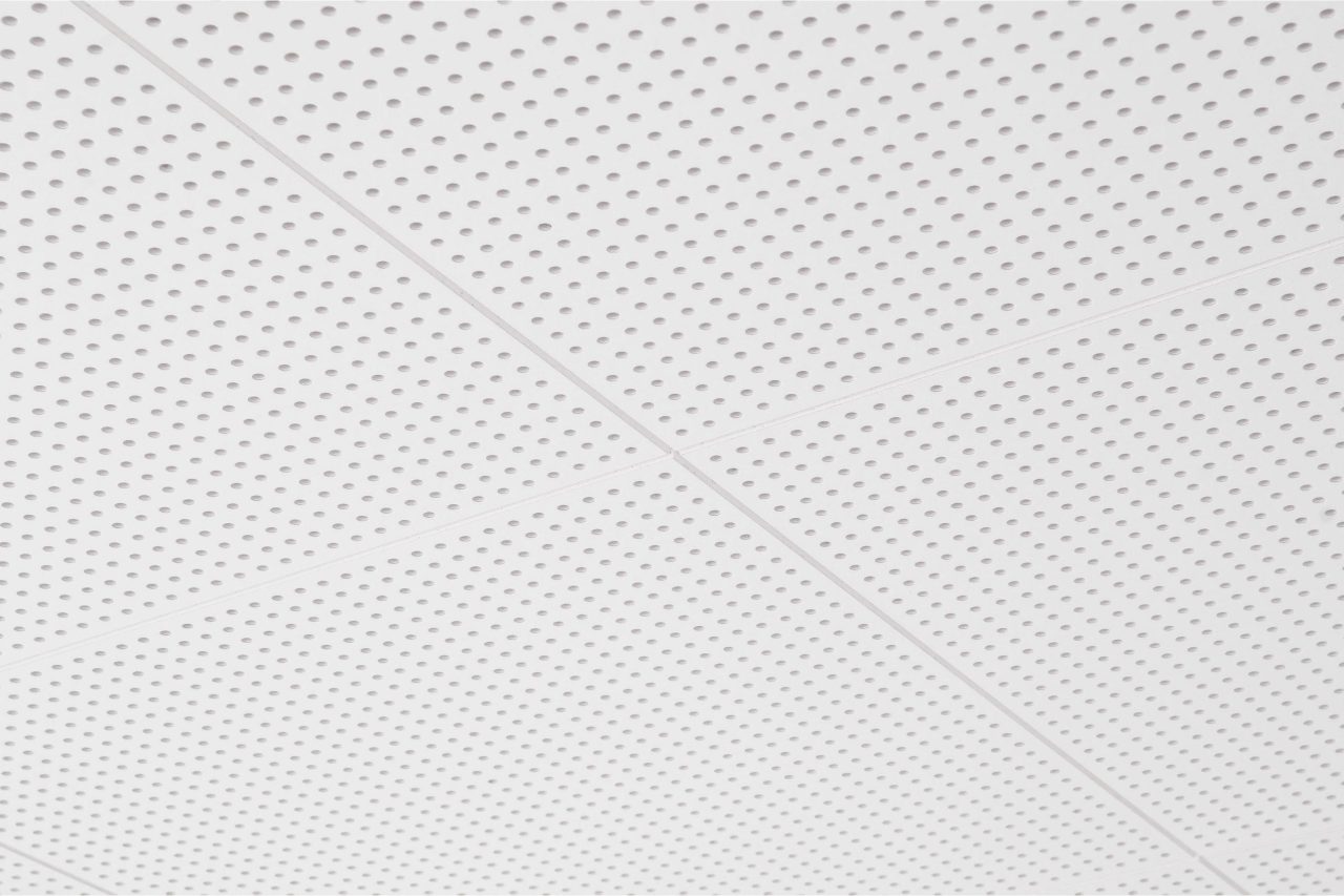 Close-up view of a white perforated ceiling with a grid pattern, showing intersecting lines and evenly spaced small round holes on each ceiling panel.