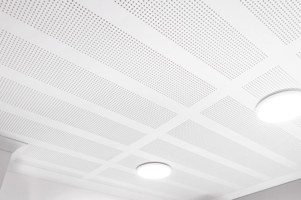 A white, perforated ceiling with a grid pattern and two round, recessed light fixtures glowing softly. The image is bright and minimalistic.