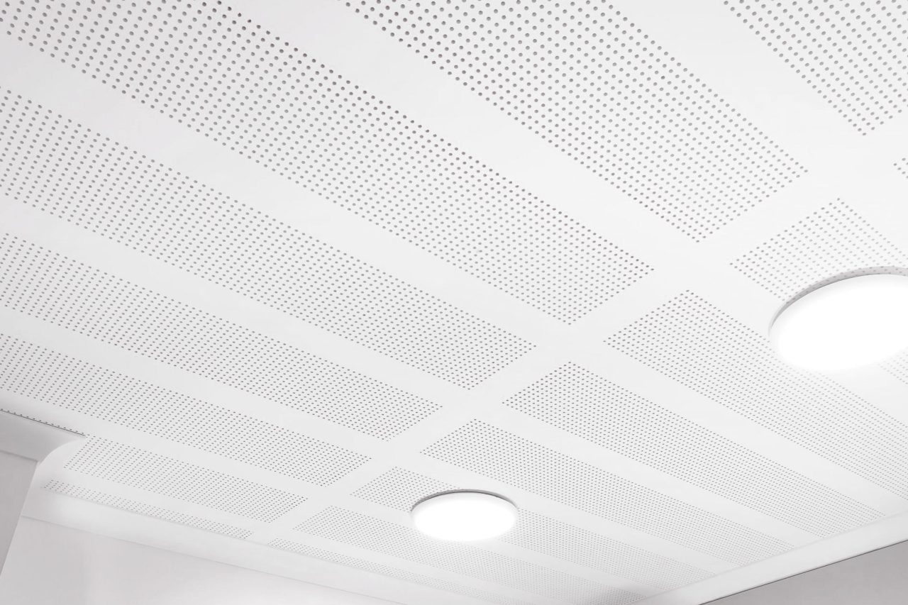 A white, perforated ceiling with a grid pattern and two round, recessed light fixtures glowing softly. The image is bright and minimalistic.