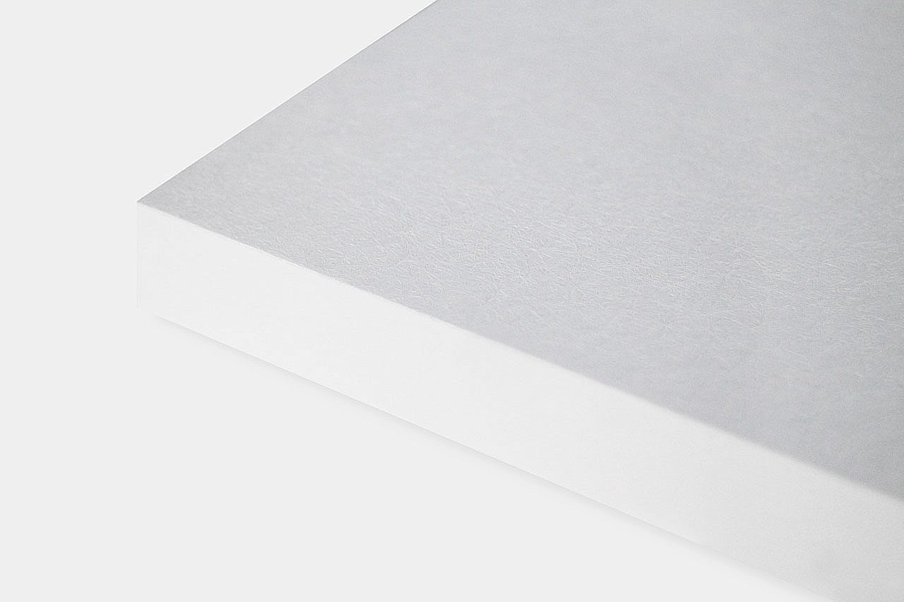 A close-up of the corner of a white, rectangular sheet of paper or cardstock on a plain light background. The surface shows a subtle, textured finish.