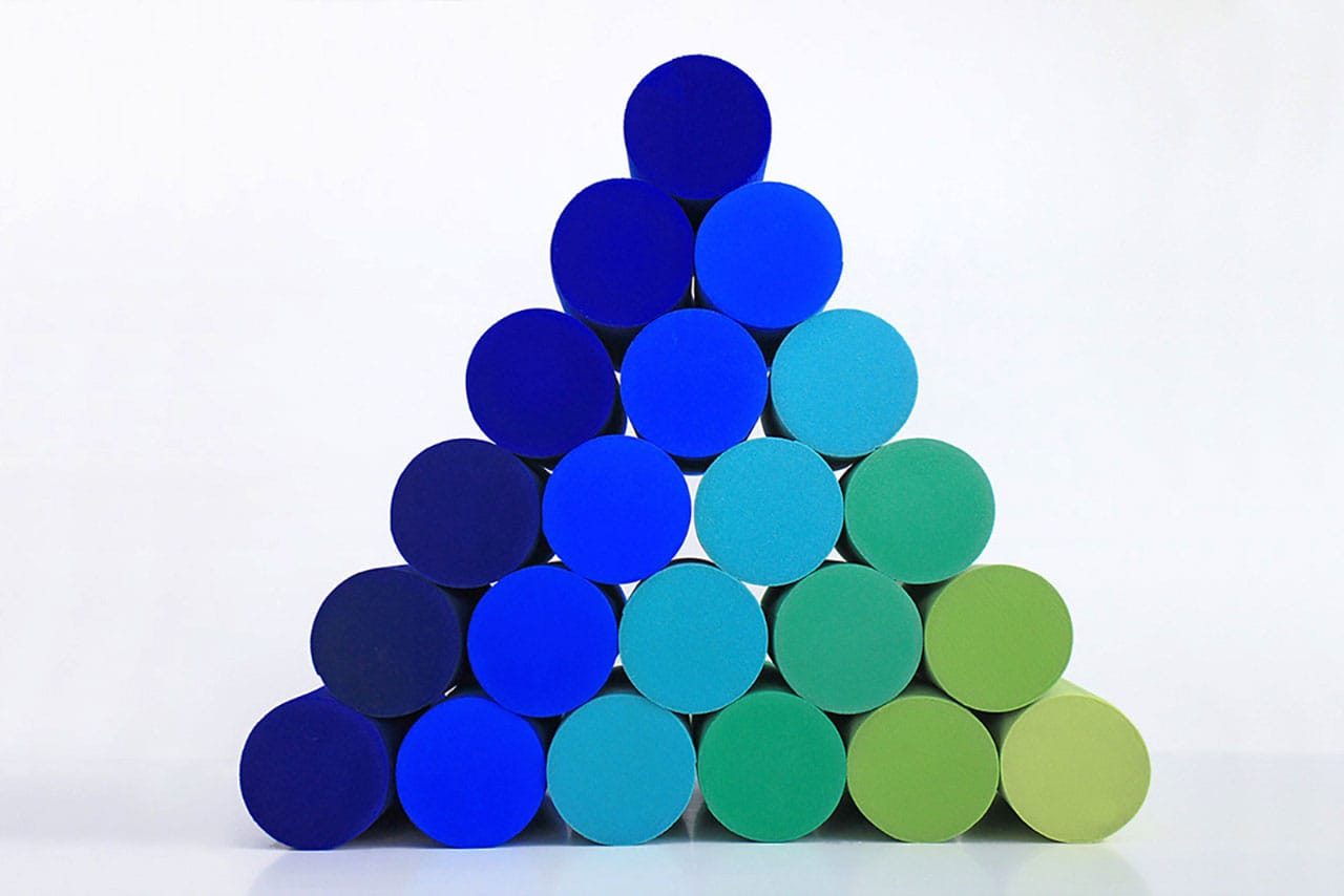 A pyramid made of colored cylinders in shades of blue and green is stacked against a white background. The colors transition from deep blue at the top to green at the bottom right.