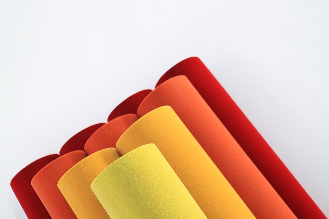 Several sheets of textured paper or material in shades of yellow, orange, and red are rolled up and arranged diagonally against a plain white background.