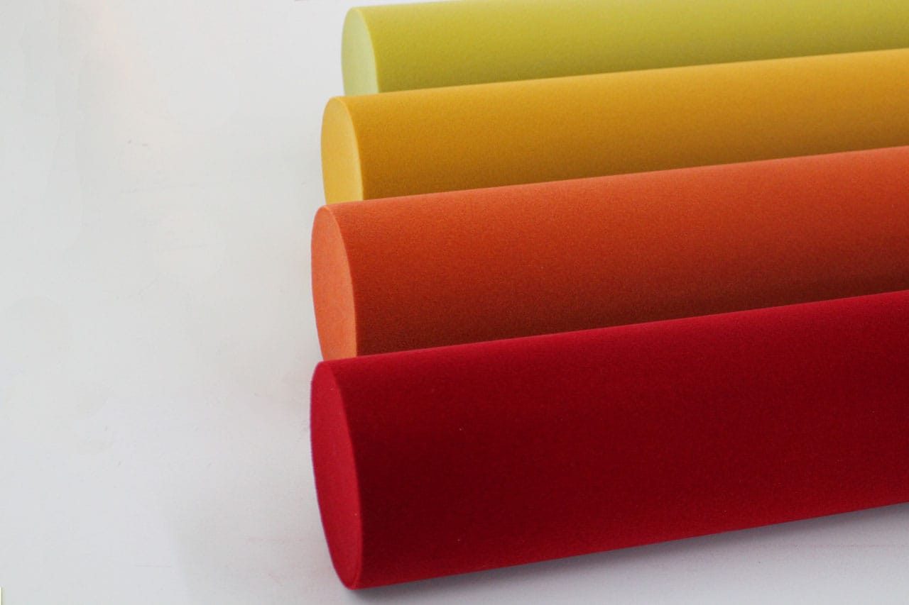 Four cylindrical foam shapes in red, orange, yellow-orange, and light yellow are arranged parallel to each other on a white surface.