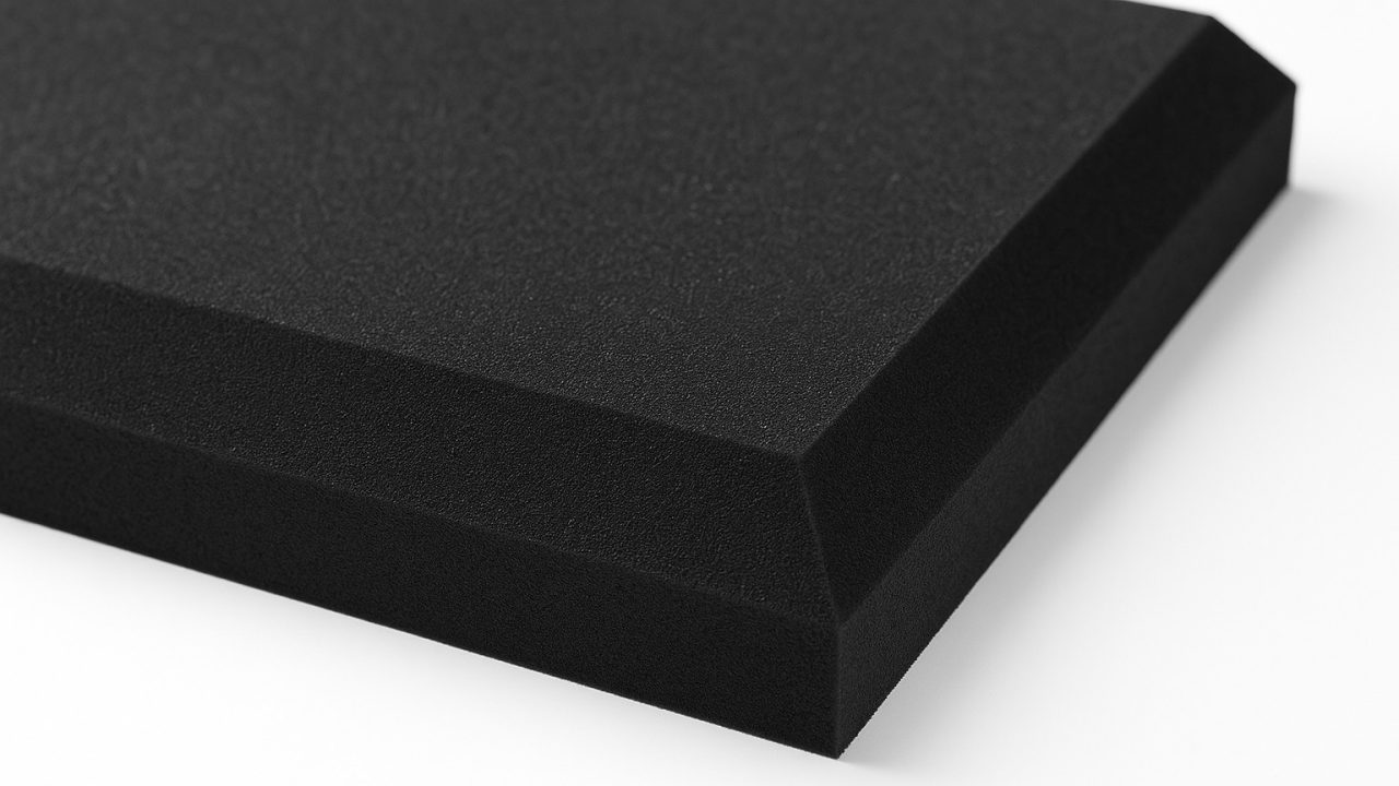 A close-up of a rectangular piece of black foam with squared edges and a beveled side, photographed against a white background.