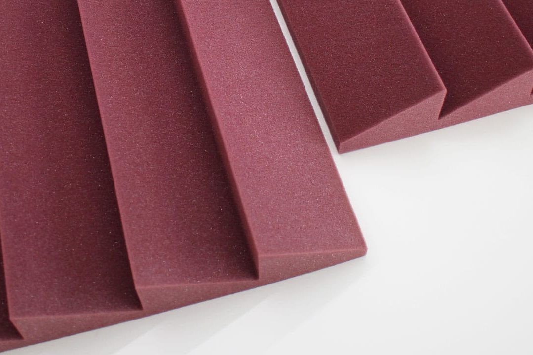 Close-up view of maroon-colored acoustic foam panels with ridged, triangular patterns arranged on a white surface.