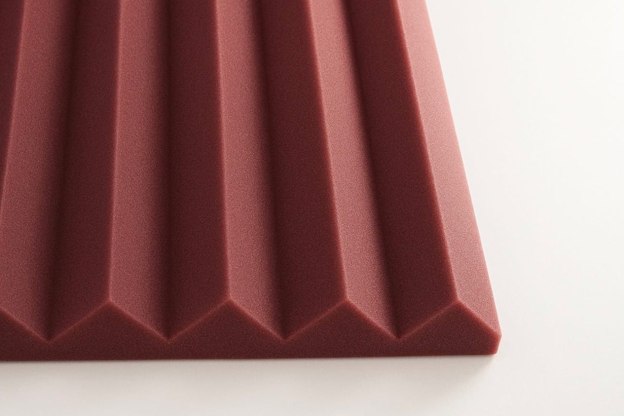 Close-up view of a maroon acoustic foam panel with a series of evenly spaced, triangular ridges, placed on a white surface.