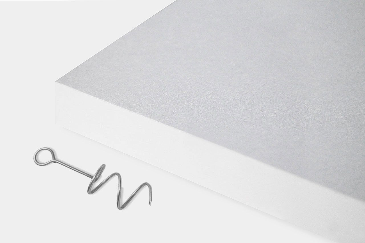 A silver corkscrew lies next to the lower right corner of a thick, white rectangular sheet or board on a plain white background.