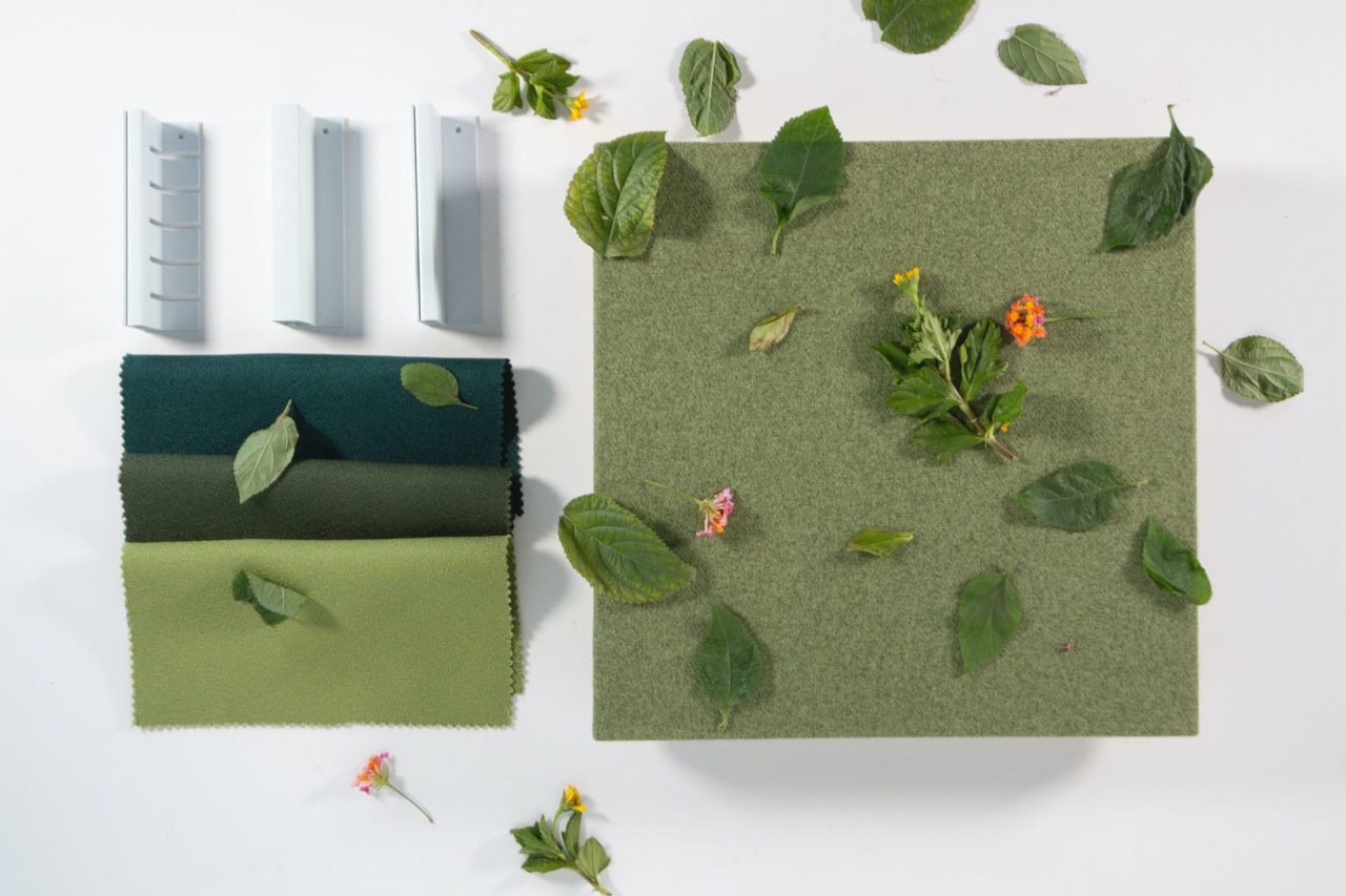 A green fabric square, scattered with leaves and small flowers, sits beside three rectangular gray samples and two fabric swatches—one dark green, one light green—on a white background.
