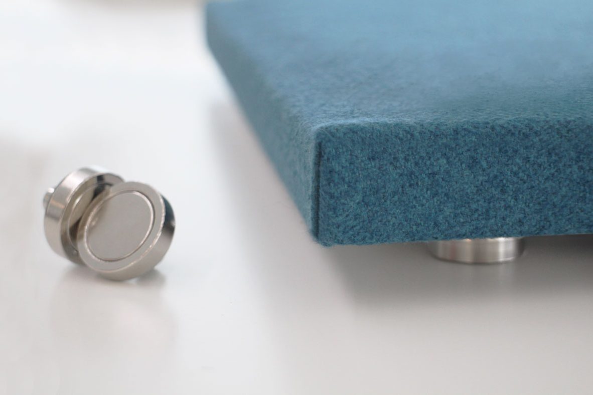 A close-up of a blue, fabric-covered object on metal feet, with a small, round silver knob or fastener placed nearby on a white surface.