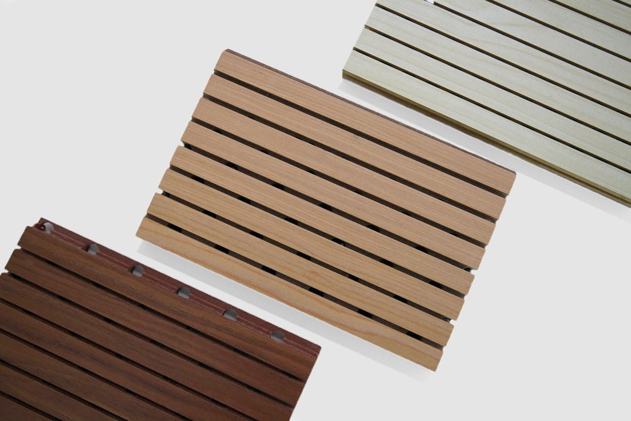 Three rectangular wooden slatted panels in different wood tones—light, medium, and dark—are arranged diagonally on a plain white background.