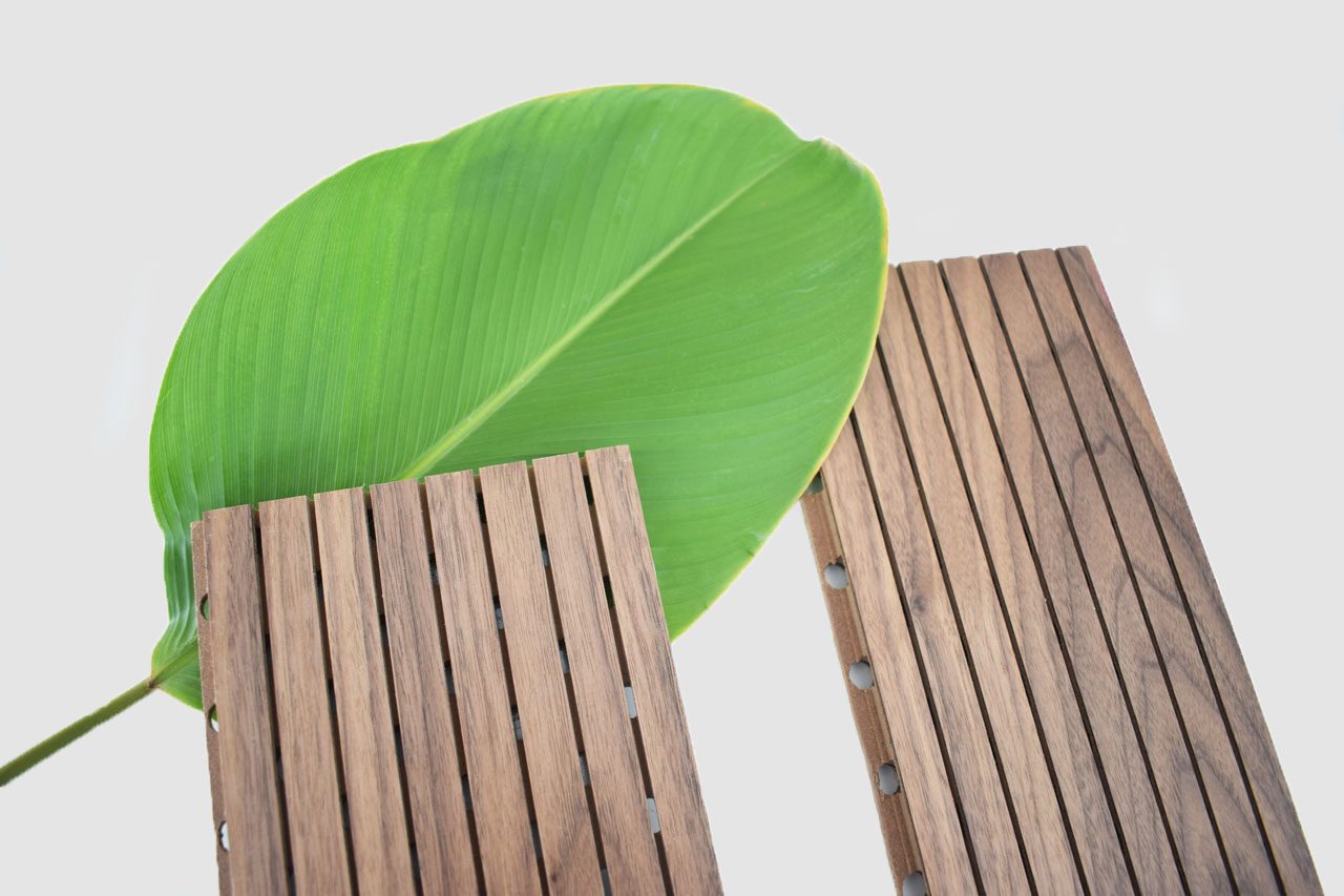 A large green leaf is placed behind two rectangular wooden panels with vertical grooves, all set against a plain light background.