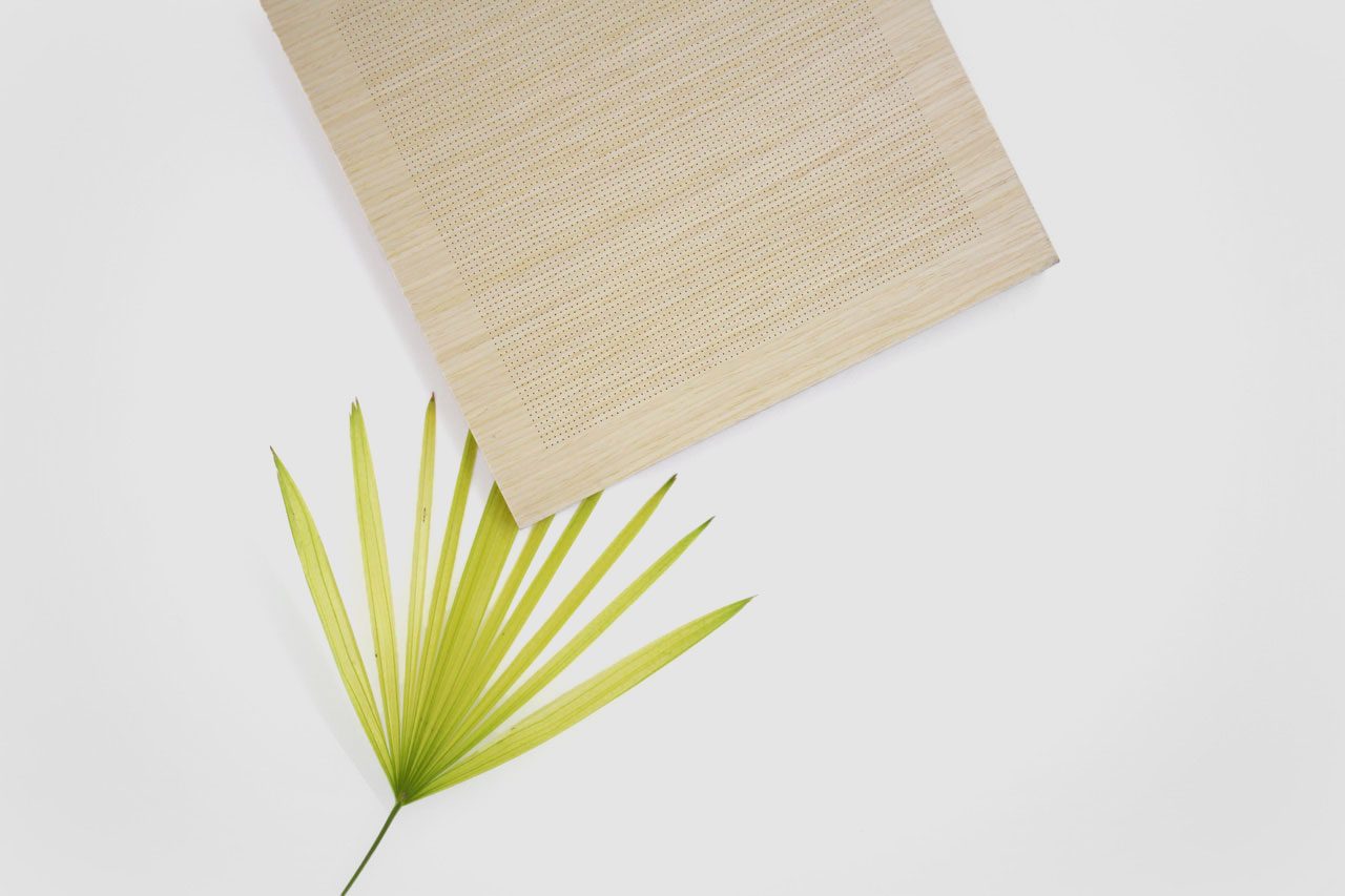 A light green palm leaf and a square beige woven mat are arranged on a white background, creating a minimal and natural composition.