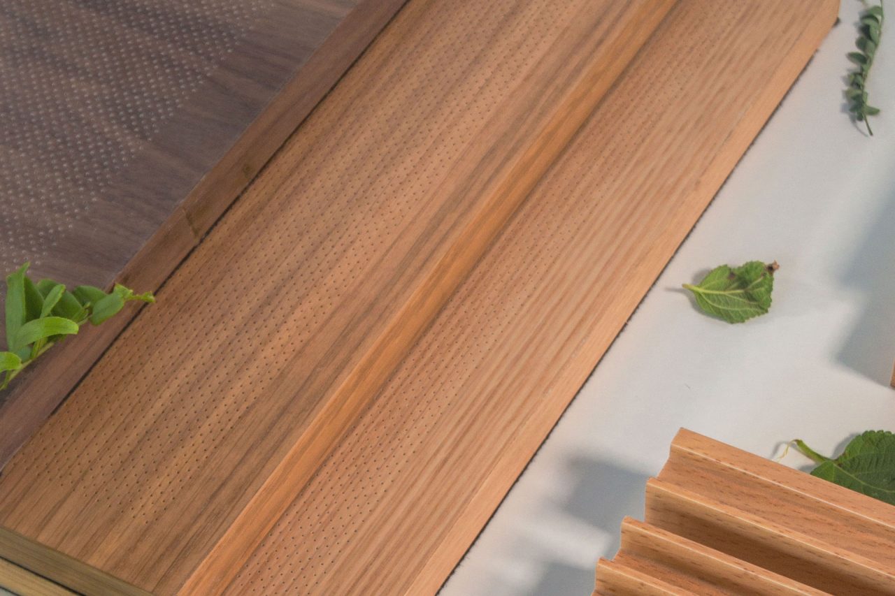 A close-up of wooden panels with fine perforated dot patterns, displayed on a light surface with green leaves placed around for decoration.