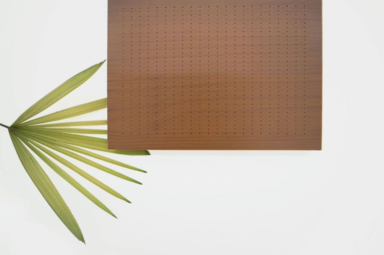 A brown rectangular perforated board on a white background, positioned in the top right corner, with a green palm leaf splayed out in the bottom left.