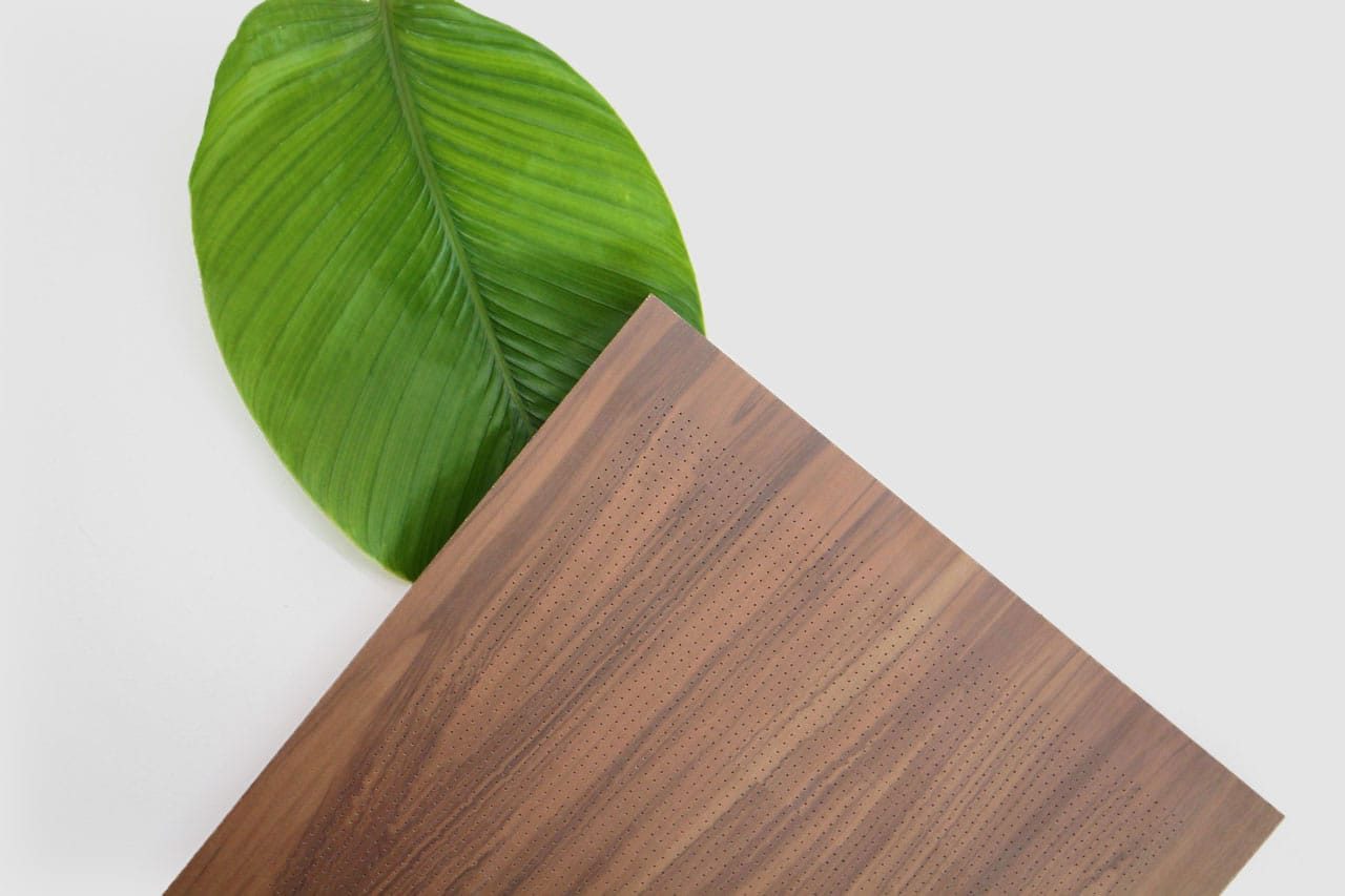 A large green tropical leaf partially covered by the corner of a rectangular wooden object with a smooth, polished surface, set against a plain white background.
