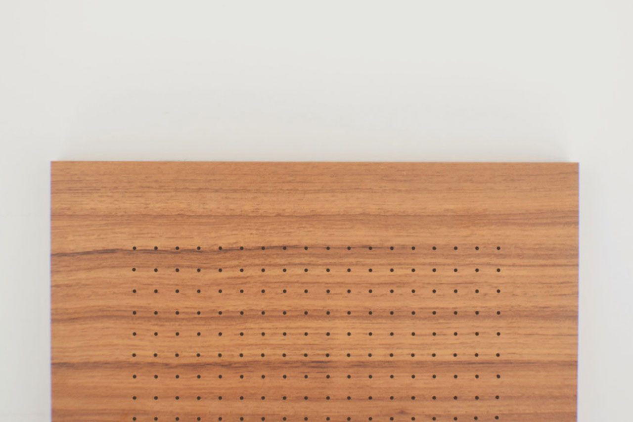 A rectangular piece of wood with evenly spaced small holes arranged in a grid pattern, positioned against a plain white background.
