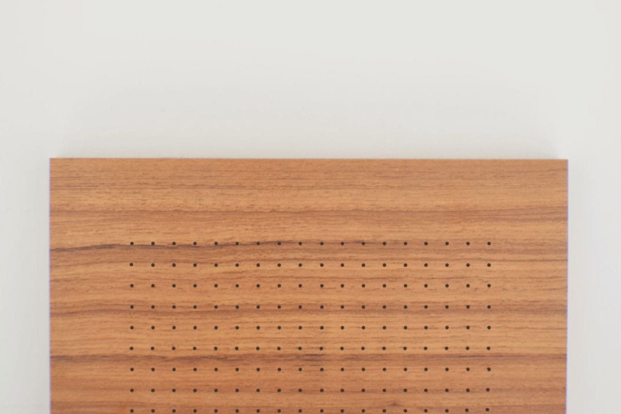 A rectangular piece of wood with evenly spaced small holes arranged in a grid pattern, positioned against a plain white background.