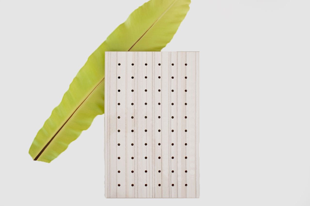 A large green leaf is placed diagonally behind a rectangular block of light-colored wood with evenly spaced holes, against a white background.