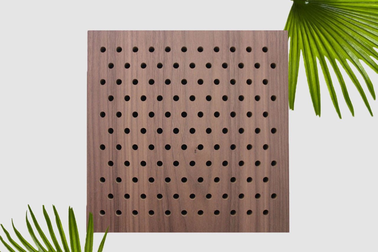 A square wooden panel with evenly spaced circular holes arranged in a grid pattern, set against a light background with green palm leaves in the top right and bottom left corners.