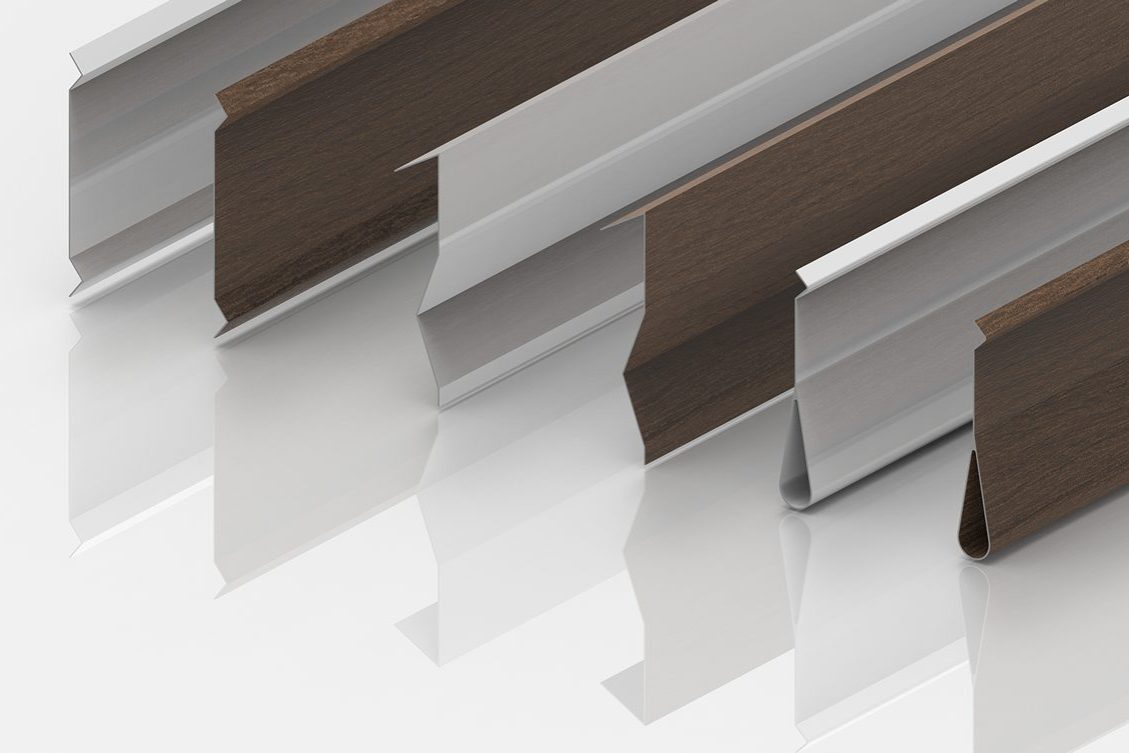 Five metal strips with angled, grooved profiles, some appearing silver and others brown with a wood-like texture, are arranged diagonally on a glossy white surface, casting soft reflections.