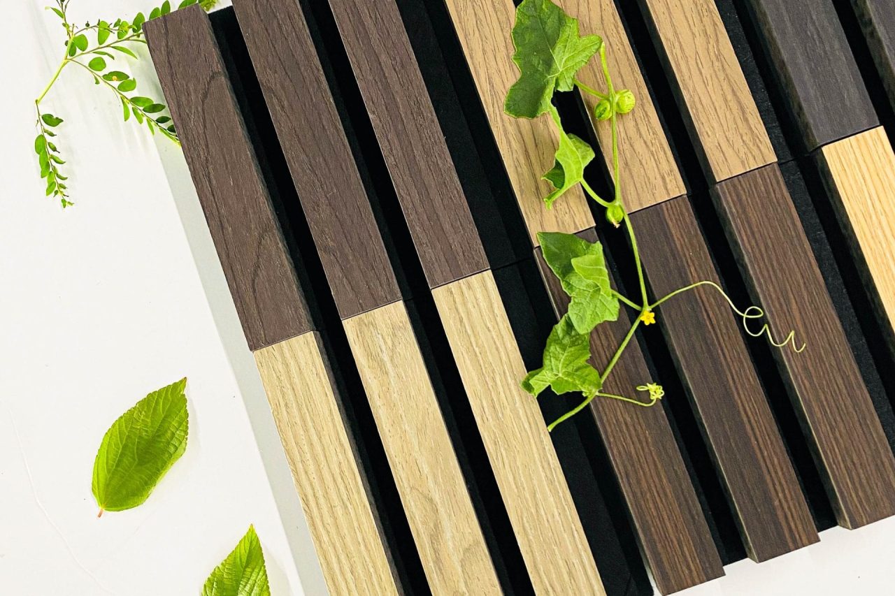 A pattern of alternating dark and light wooden slats arranged vertically, with green leaves and vines placed on and around the wood on a white surface.