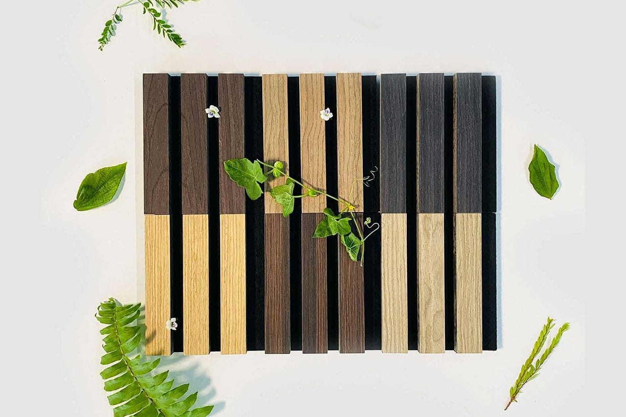 A wooden trivet with alternating dark and light slats, decorated with green leaves, small white flowers, and surrounded by various leaves and plants on a light background.