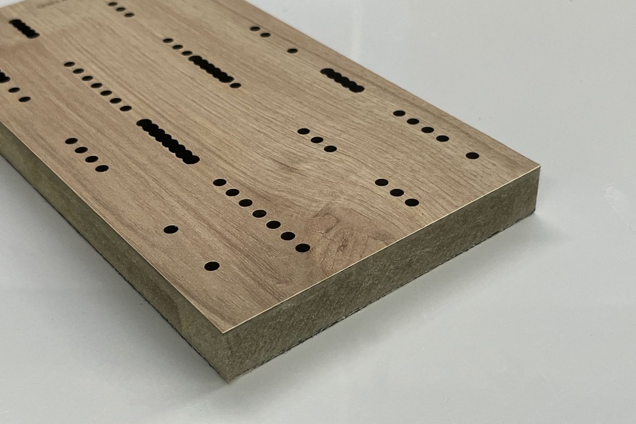 A rectangular wooden board with a light brown finish, featuring rows of neatly drilled holes and slots of varying sizes, lies on a plain white surface.