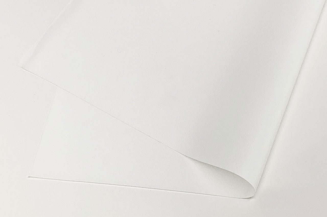 A single sheet of plain white paper lies on a white surface, slightly curled at one corner, creating soft shadows.