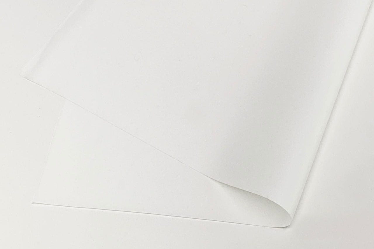 A single sheet of plain white paper lies on a white surface, slightly curled at one corner, creating soft shadows.