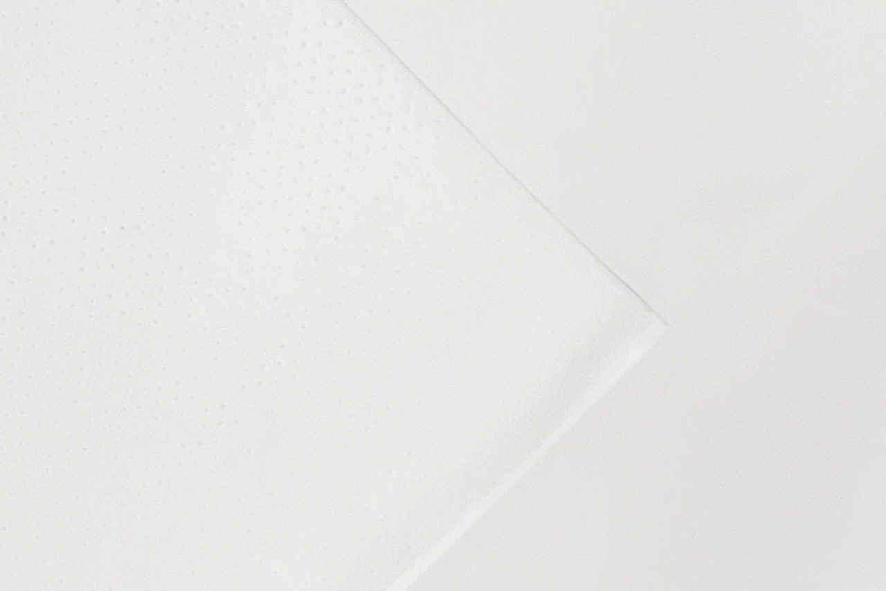 A close-up of a folded white paper napkin on a white background, with small dotted texture visible on part of the napkin.