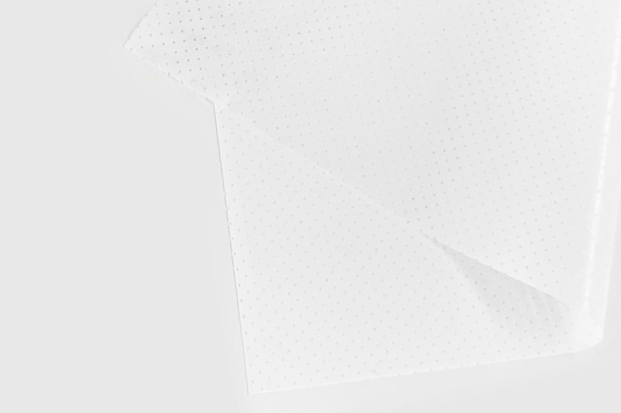 A close-up of two overlapping sheets of translucent, white, perforated material on a plain white surface. The small, evenly spaced holes give a dotted pattern to the sheets.