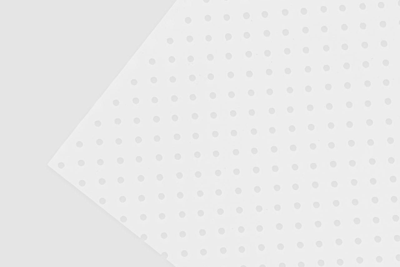 A white sheet with evenly spaced small circular holes is laid diagonally on a light gray background, creating a geometric pattern with subtle shadows and a minimalist design.