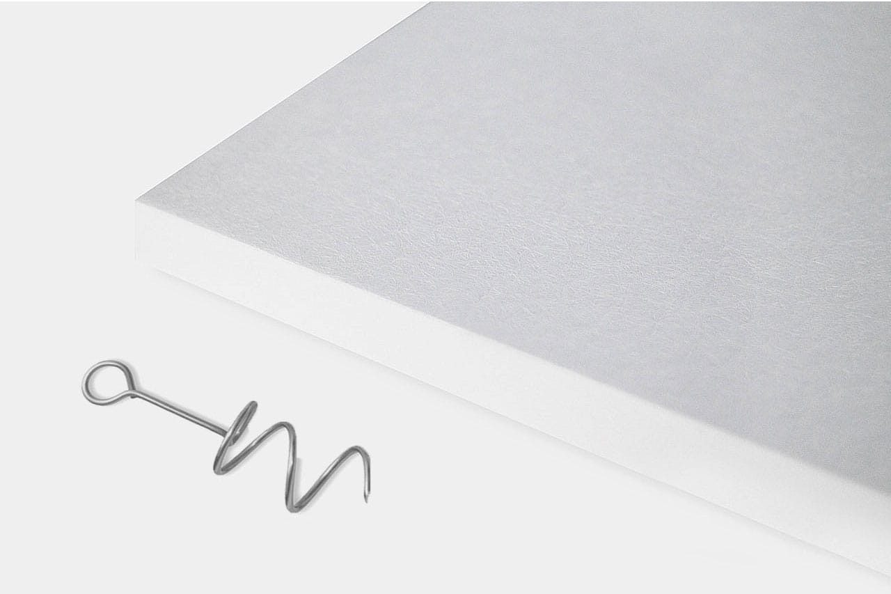 A metal corkscrew lies next to the corner of a thick white rectangular board on a plain white background.