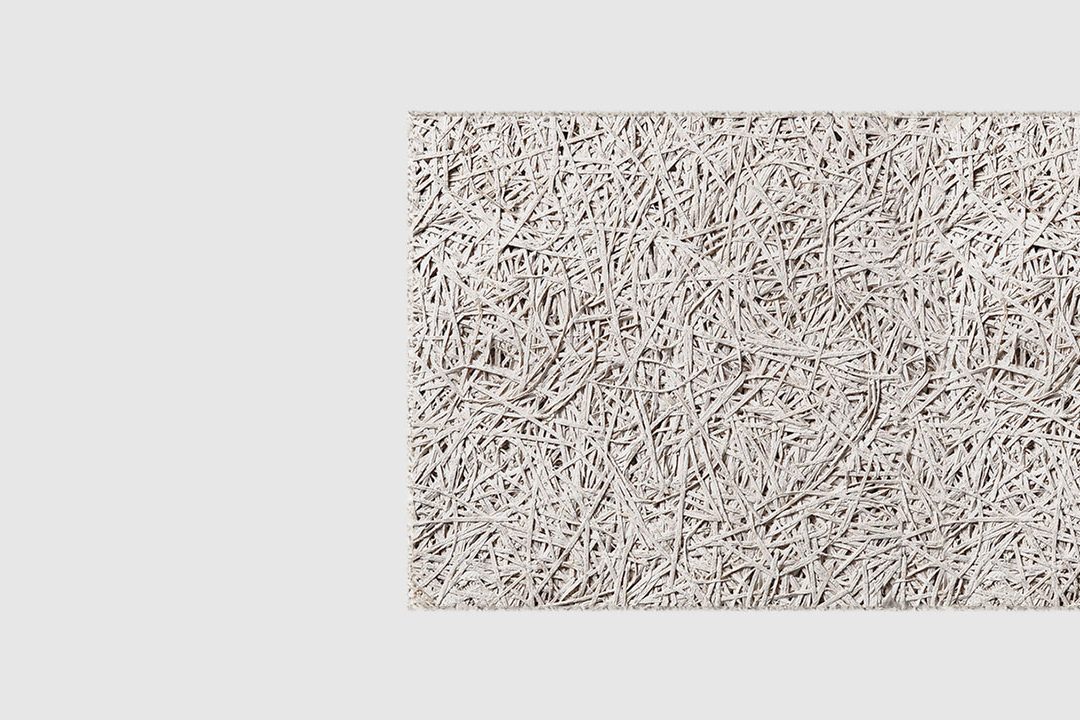 A close-up view of a textured, light grey rectangular panel made of compressed wood fibers on a plain white background.