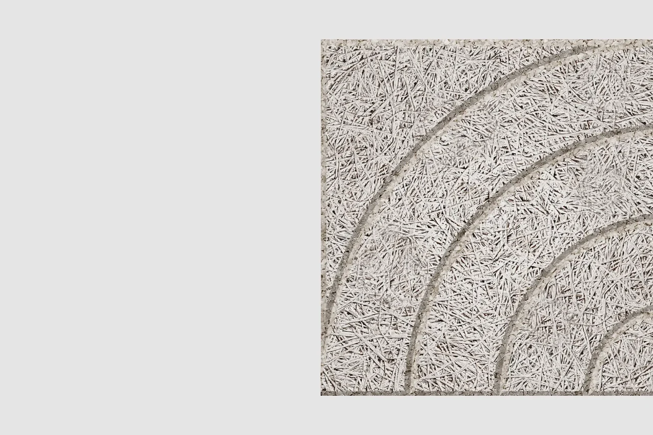 A textured beige panel with curved, raised lines forming an abstract arch pattern; the surface resembles compressed straw or wood fibers. The panel is set against a plain light gray background.