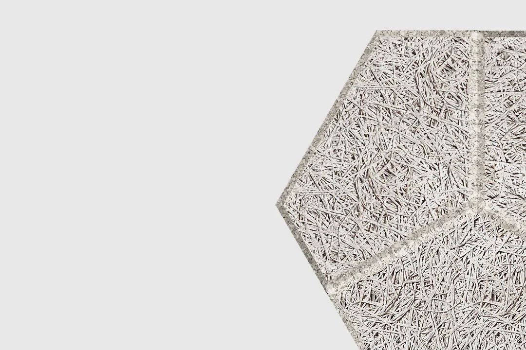 A close-up of a textured, light gray hexagonal panel made of intertwined wood fibers, positioned against a plain white background.